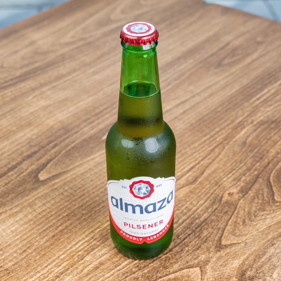 Chilled green Almaza Pilsener beer bottle standing on a wooden restaurant table.