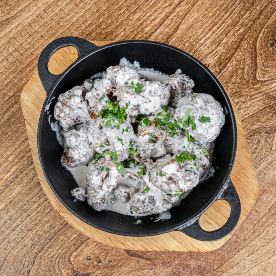 Skillet of meatballs covered in creamy white sauce and chopped parsley on a wooden serving board.