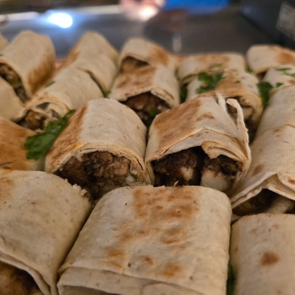 Grilled meat-filled wraps arranged on a platter, with toasted flatbread, herbs, and browned fillings visible.