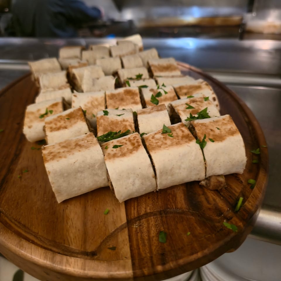 Grilled flatbread rolls cut into bite-sized pieces and garnished with chopped herbs on a wooden serving board.