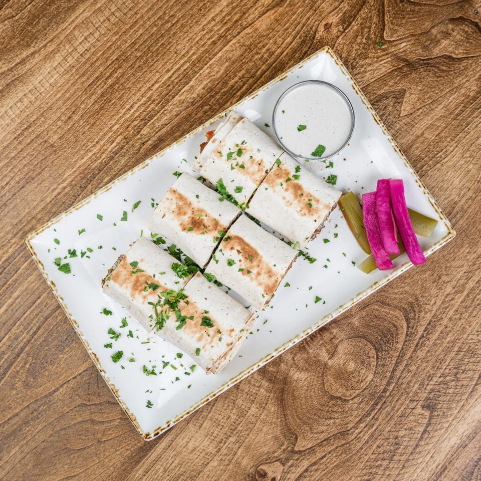Grilled tortilla wraps garnished with chopped herbs, served with creamy dipping sauce, pickles, and pickled vegetables on a white plate.