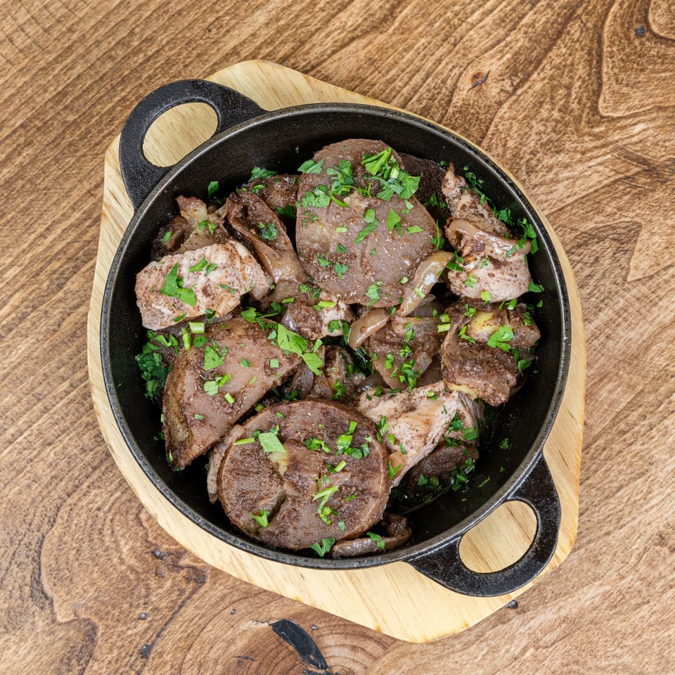 Skillet filled with grilled meat pieces, onions, and chopped parsley on a wooden serving board and rustic table.