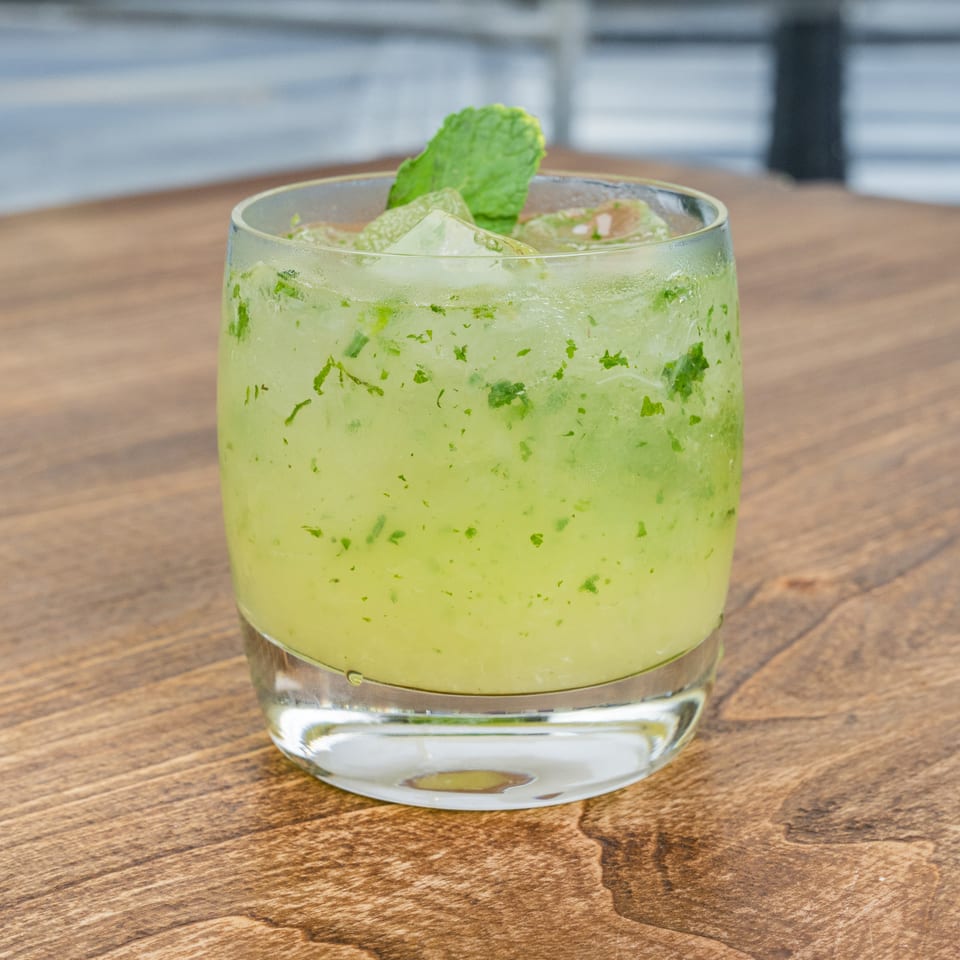 Refreshing mint cocktail with crushed ice in a tumbler on a wooden restaurant table.