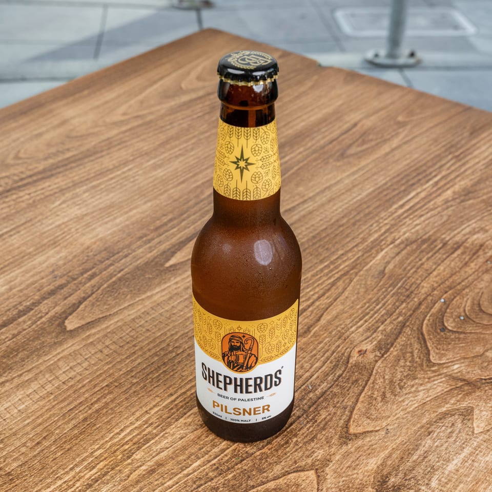 Bottle of Shepherds Pilsner beer from Palestine standing on a wooden table.