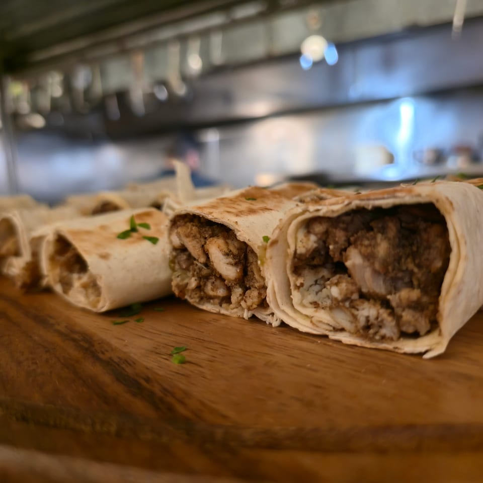Sliced meat-filled wraps garnished with parsley on a wooden serving board in a softly lit restaurant.