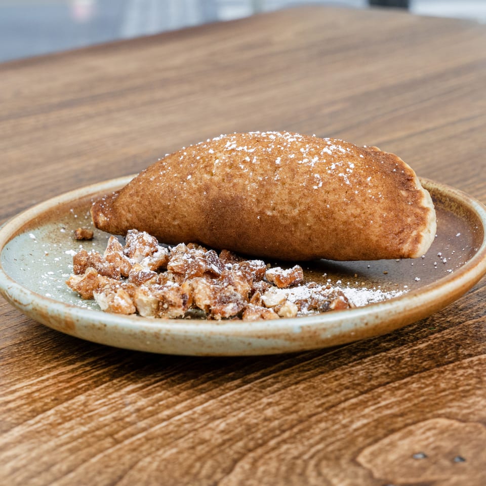 Golden-brown pastry dusted with powdered sugar, served with crumbled pieces on a ceramic plate atop a wooden table.