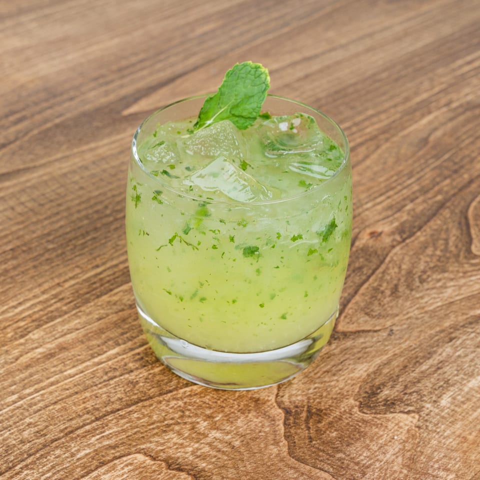 Green mint cocktail with crushed ice and fresh mint garnish in a glass on a wooden table.