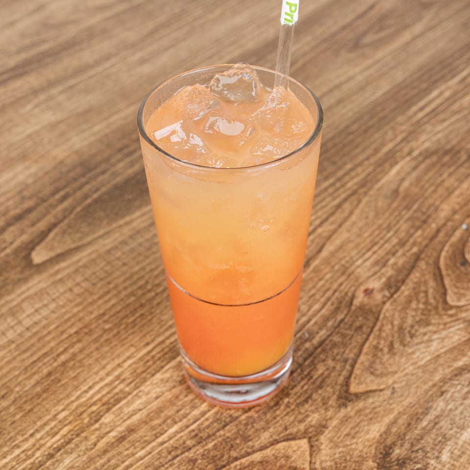 Orange iced beverage in a clear glass with a straw, resting on a wooden restaurant table.