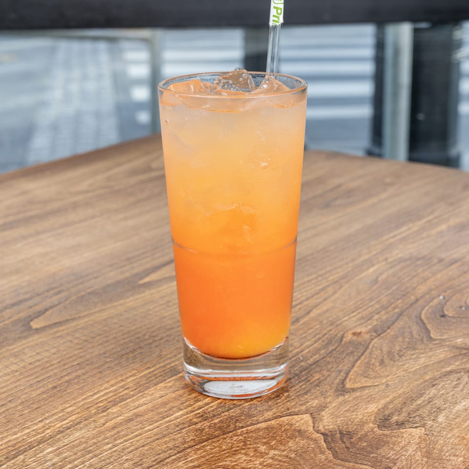 Orange iced drink with a straw served in a clear glass on a wooden restaurant table.