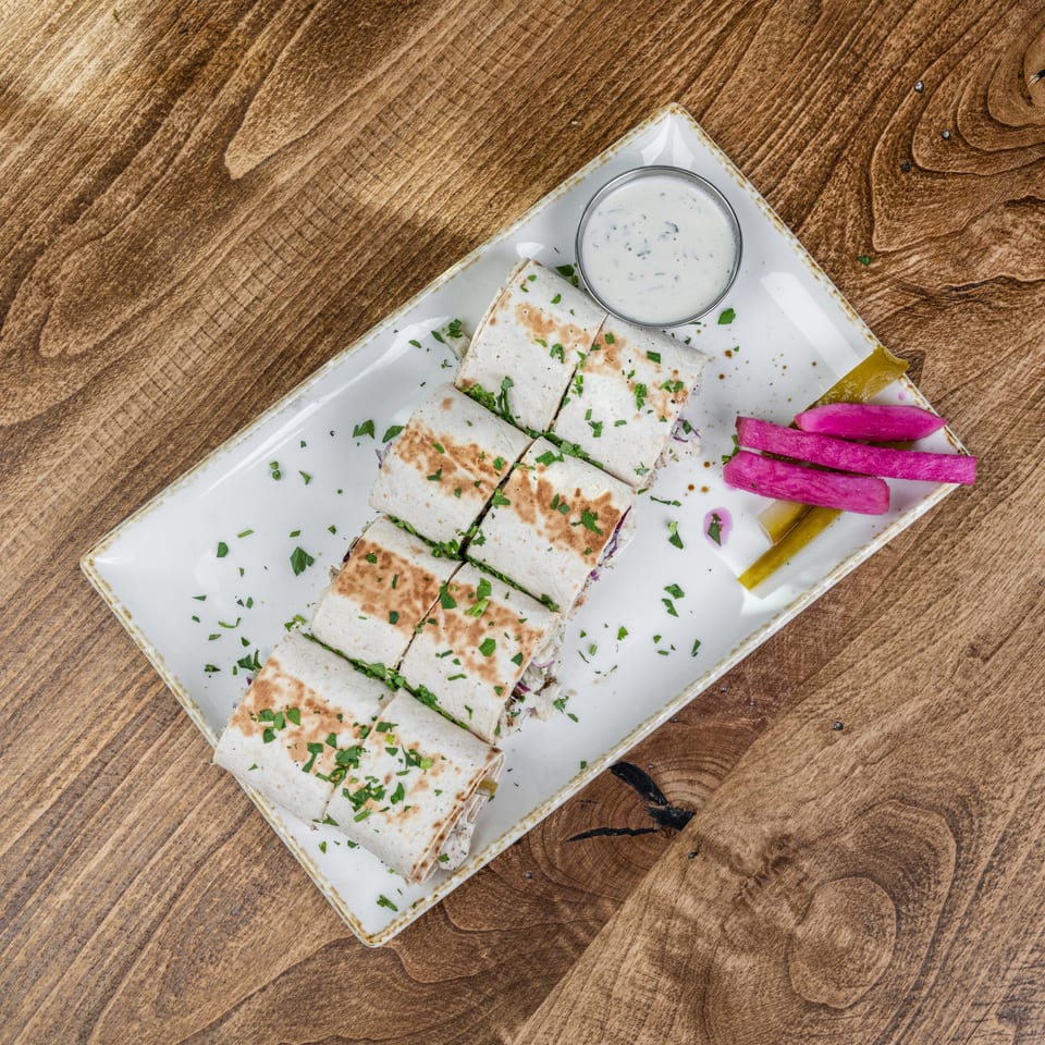 Grilled quesadilla pieces garnished with herbs, served with creamy dipping sauce, pickled radishes, and peppers on a white plate.